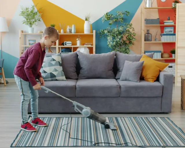 Ett litet barn dammsuger en randig matta i vardagsrummet.