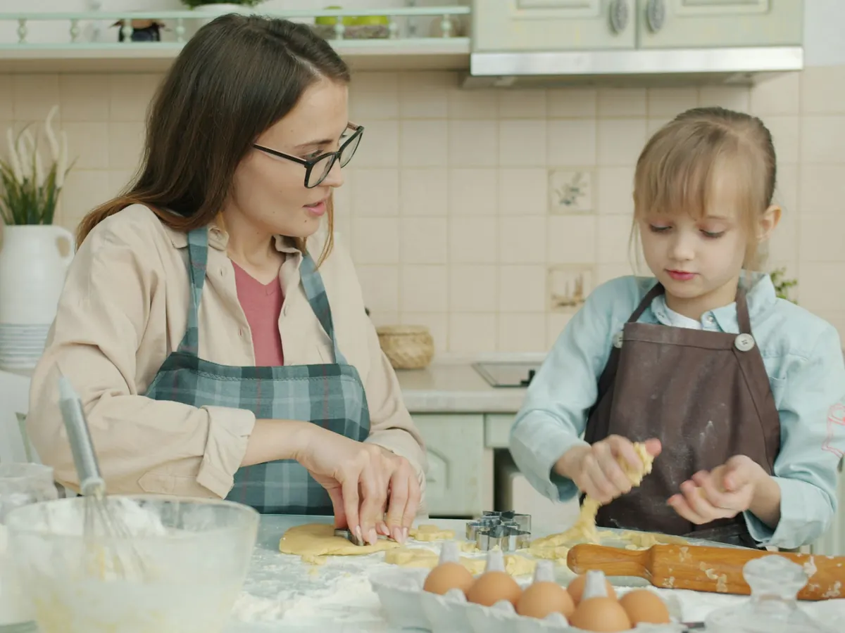 En mamma och hennes dotter tar ut kakor ur den utkavlade degen tillsammans i köket.
